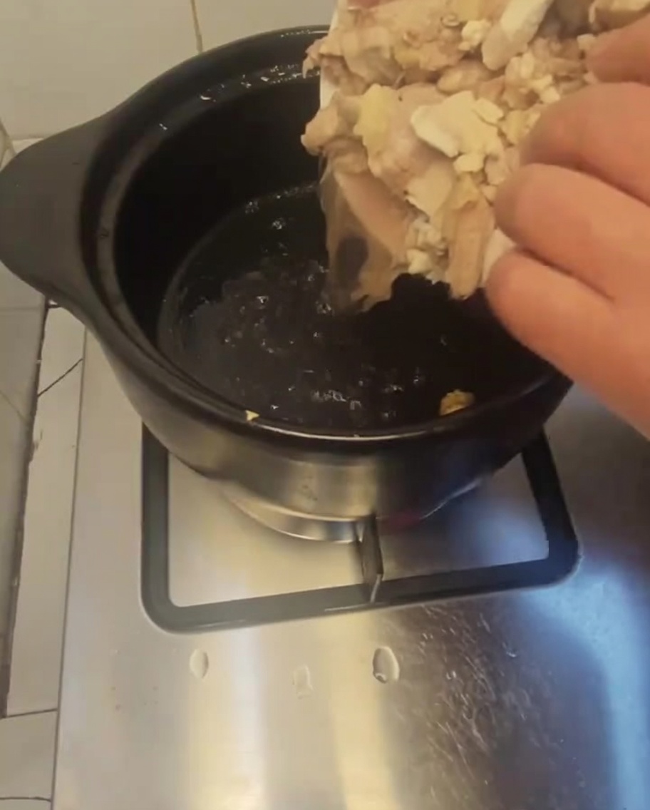白いお皿から温めた黒い土鍋に下茹でした鶏肉を入れている様子。