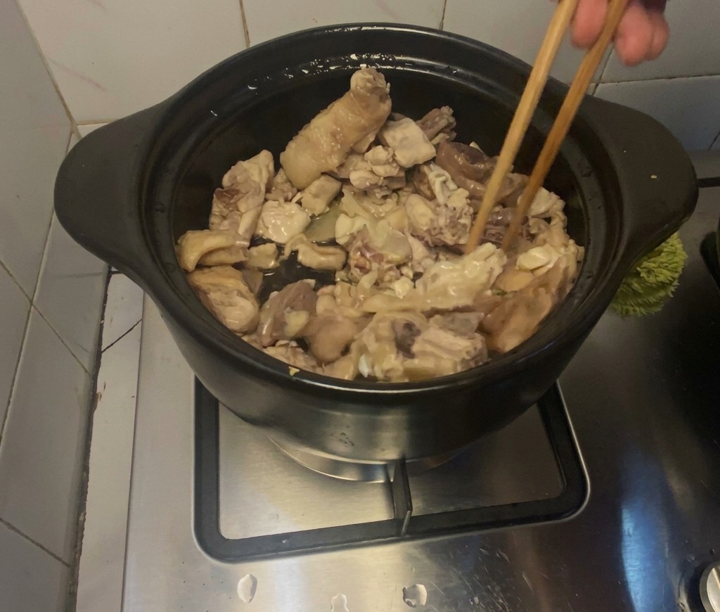 コンロに置かれた黒い土鍋の中で、菜箸を使って鶏肉を炒めている様子。