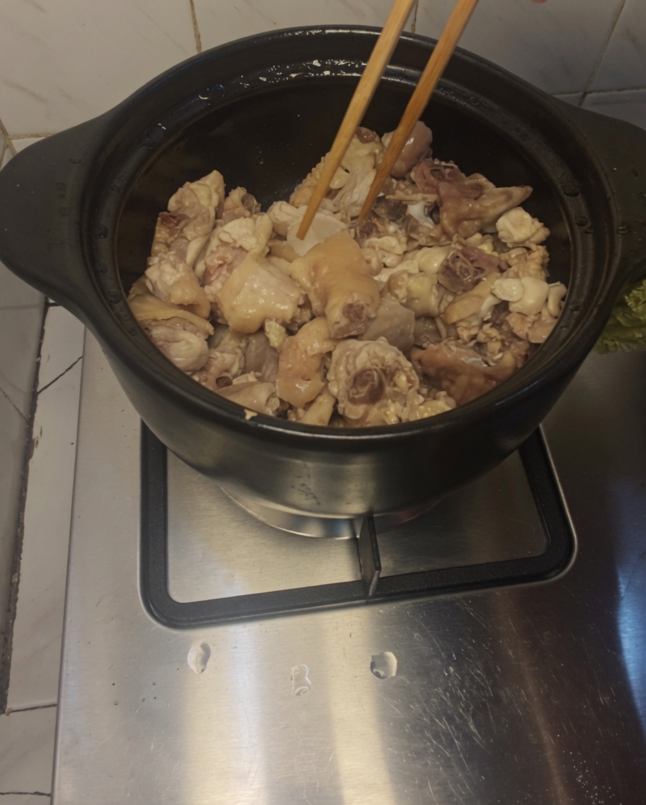 熱した土鍋の中で、鶏肉と生姜の薄切りを菜箸で炒めている様子。