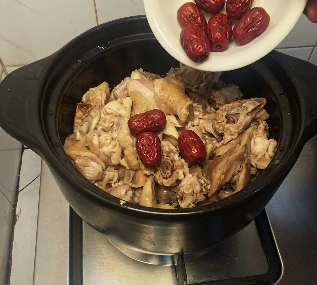 炒めた鶏肉が入った土鍋に、小皿から乾燥なつめを入れている様子。