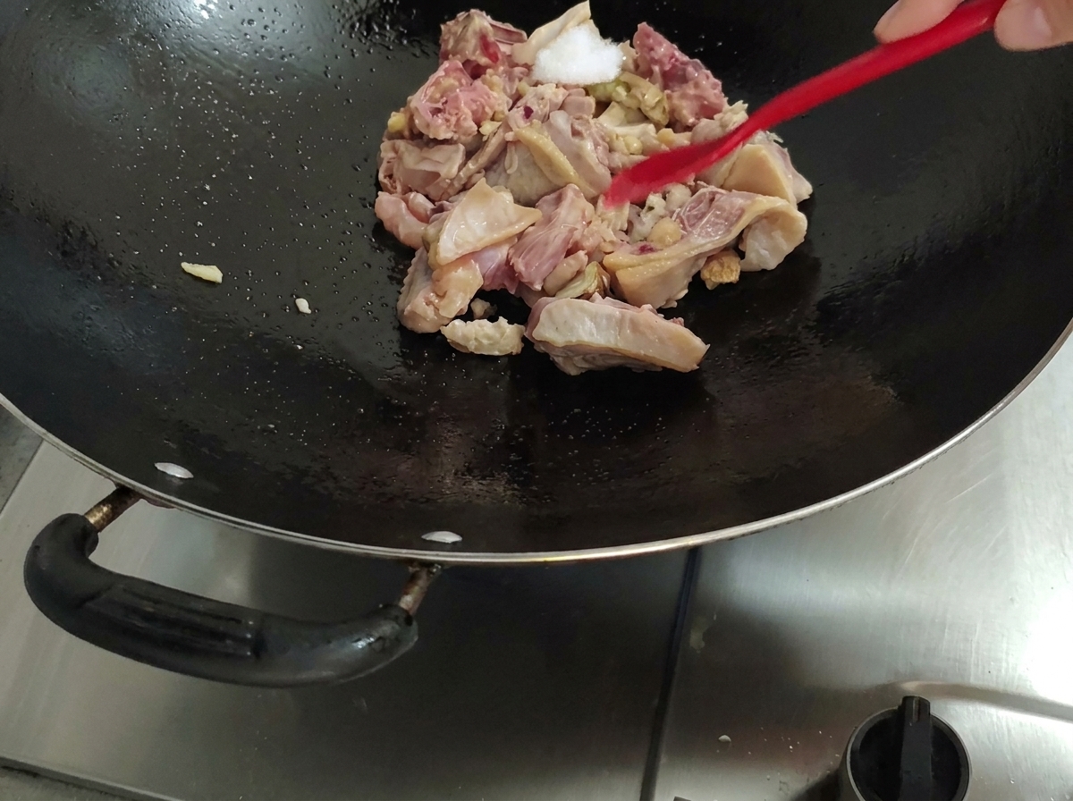 赤いヘラを使い、中華鍋の鶏肉に塩を加えている様子。