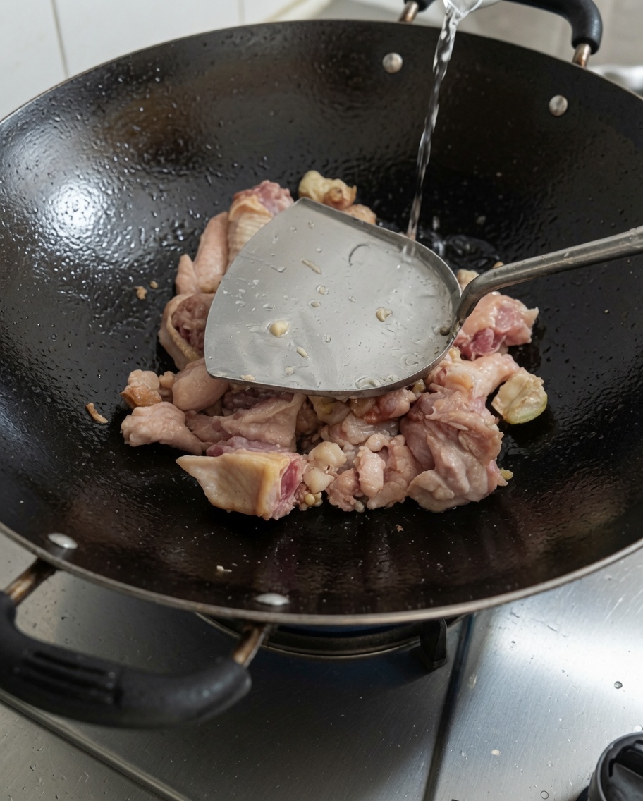 焼き色のついた鶏肉の入った中華鍋に水を注いでいる様子。