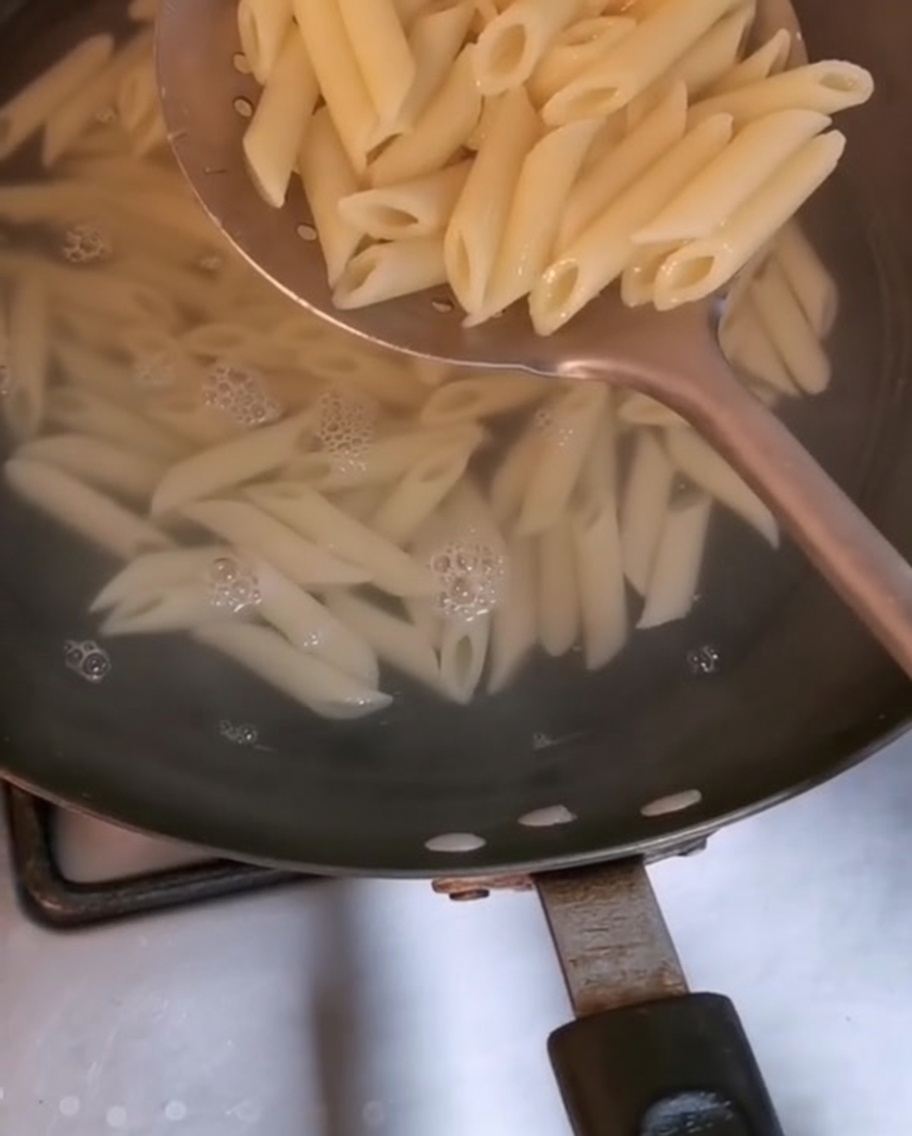 大きめの穴あきお玉で沸騰したお湯からすくい上げられるペンネ。