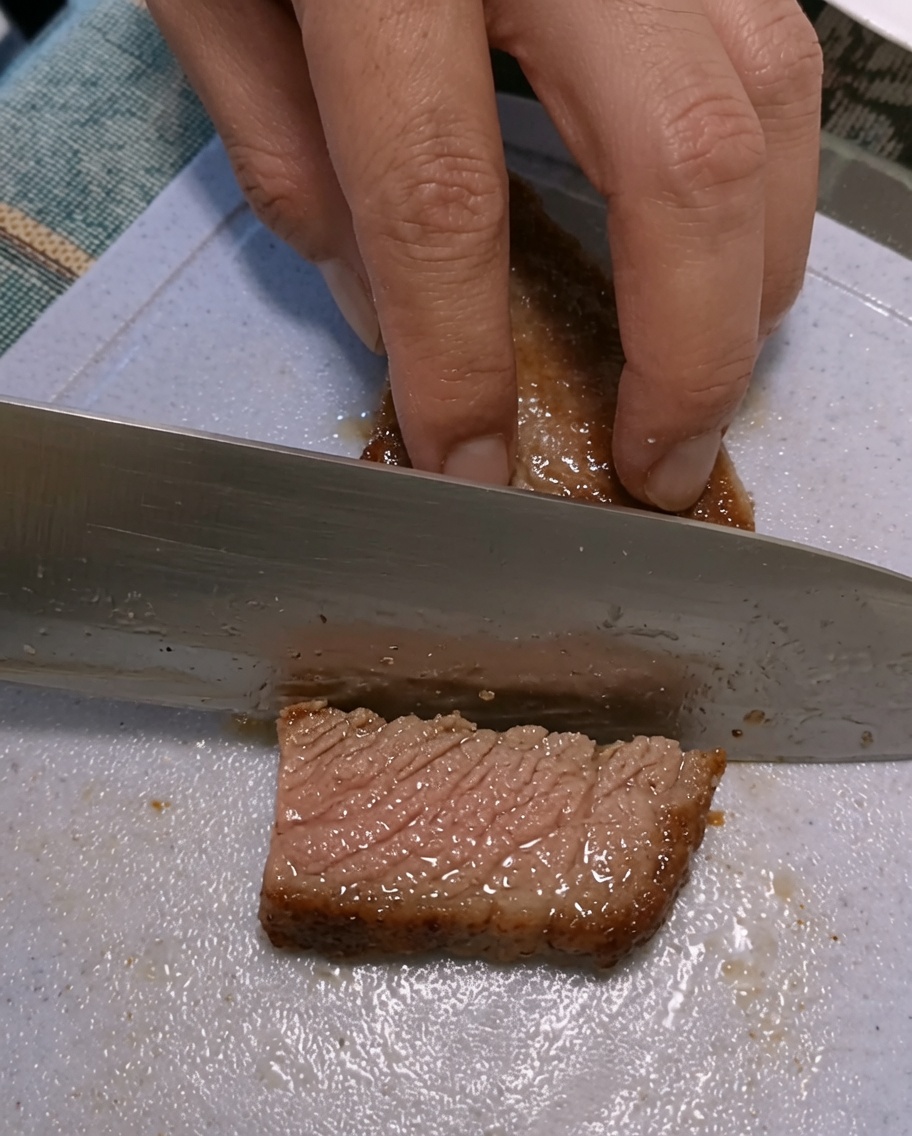 プラスチックのまな板の上で、焼いたステーキを切り分ける両手。
