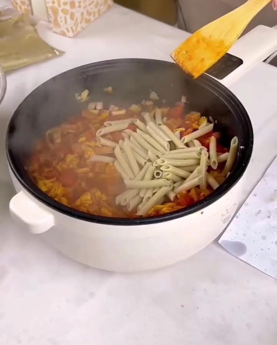 茹でたペンネをソースと具材の入ったフライパンに入れている様子。
