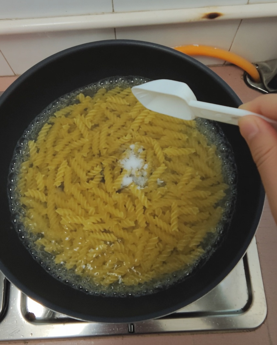 沸騰したパスタ鍋にスプーン一杯の塩を加える様子。