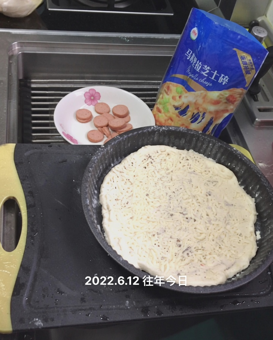 ピザ生地のホワイトソースの上にシュレッドモッツァレラチーズを振りかけている様子。