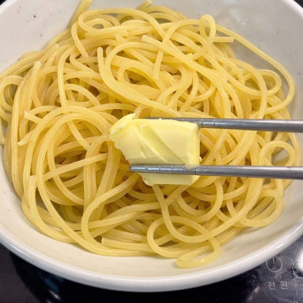 茹でたての熱いパスタが入ったボウルに、バターの塊が溶け込んでいる様子。