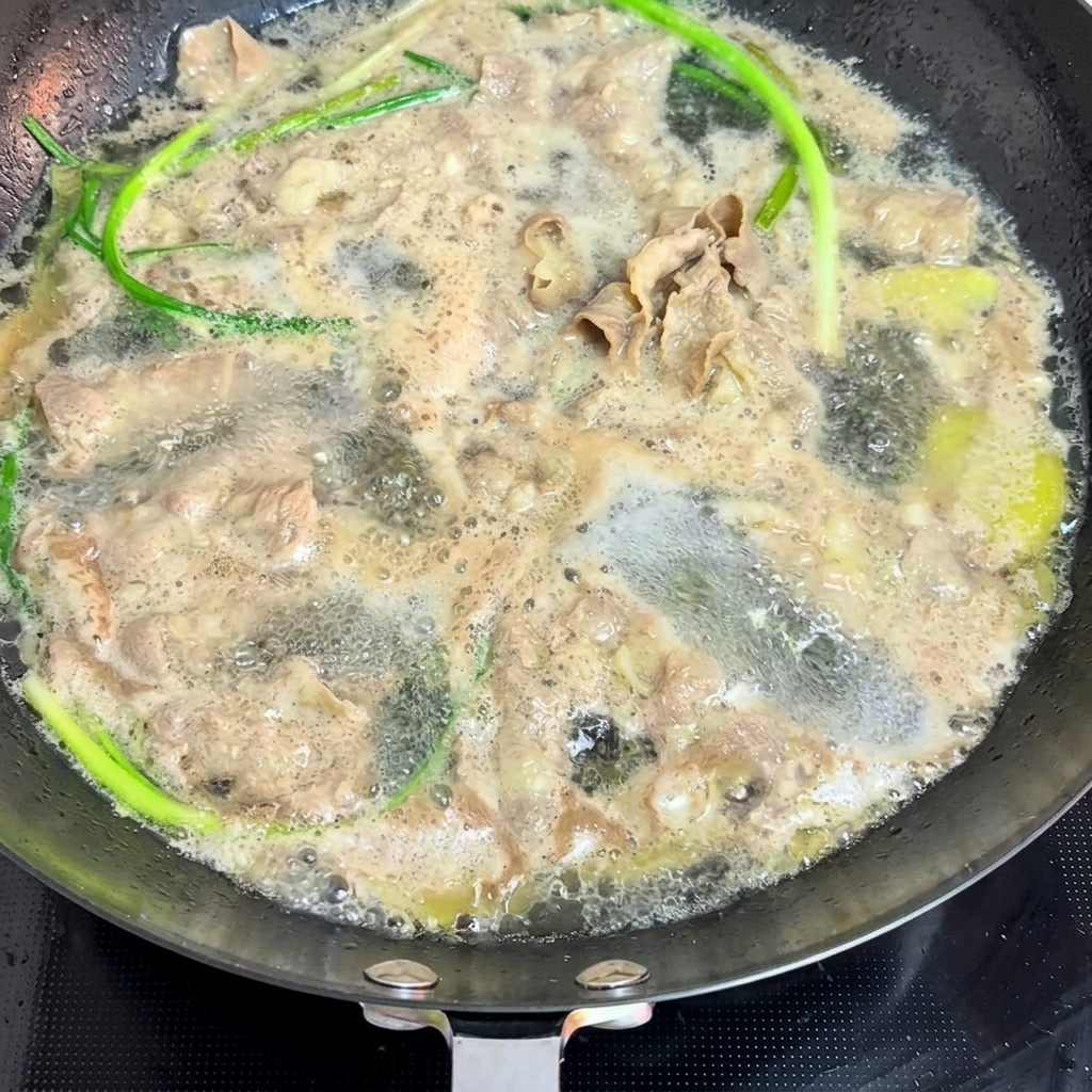 沸騰したお湯の入った鍋で、薄切りの牛肉と新鮮な青ねぎを湯通ししている様子。