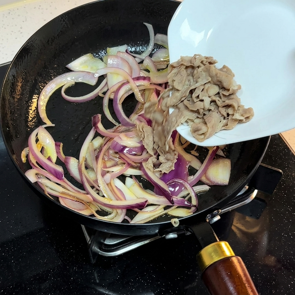 炒めた玉ねぎの入ったフライパンに、白いお皿から湯通しした牛肉を加えている様子。