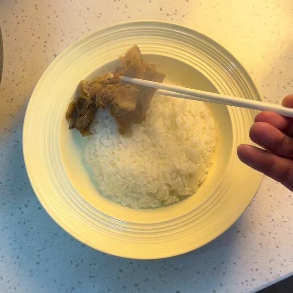 白いご飯の入った丼に、箸で調理された牛肉と玉ねぎをのせている様子。