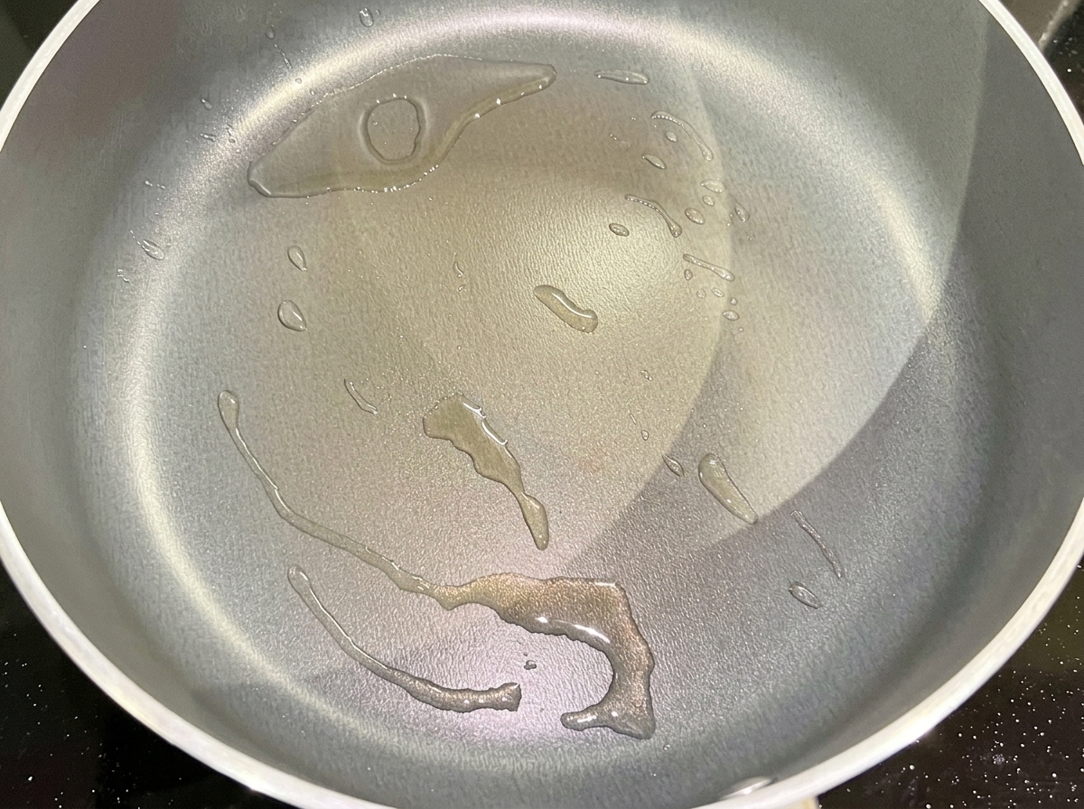 フライパンで熱した油に、刻んだ赤玉ねぎを入れて炒めている様子。