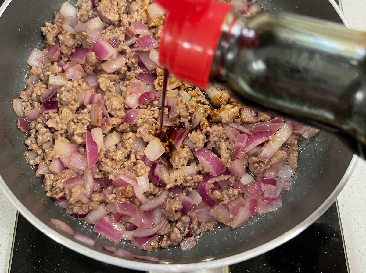 濃口醤油とケチャップを加え、ひき肉と玉ねぎに混ぜ合わせている様子。