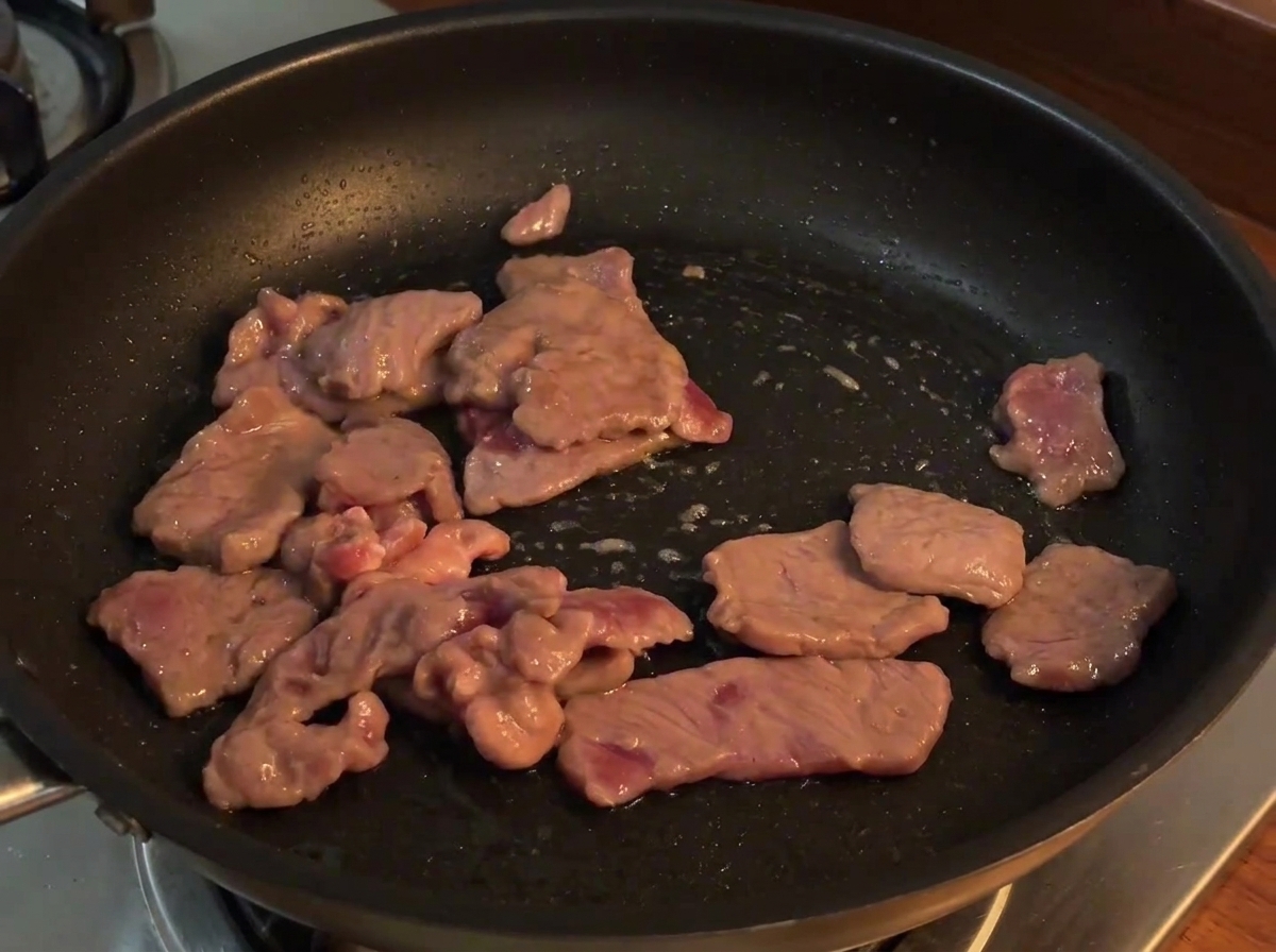 炒めた牛肉にスライスした赤玉ねぎを加えて一緒に炒めている様子