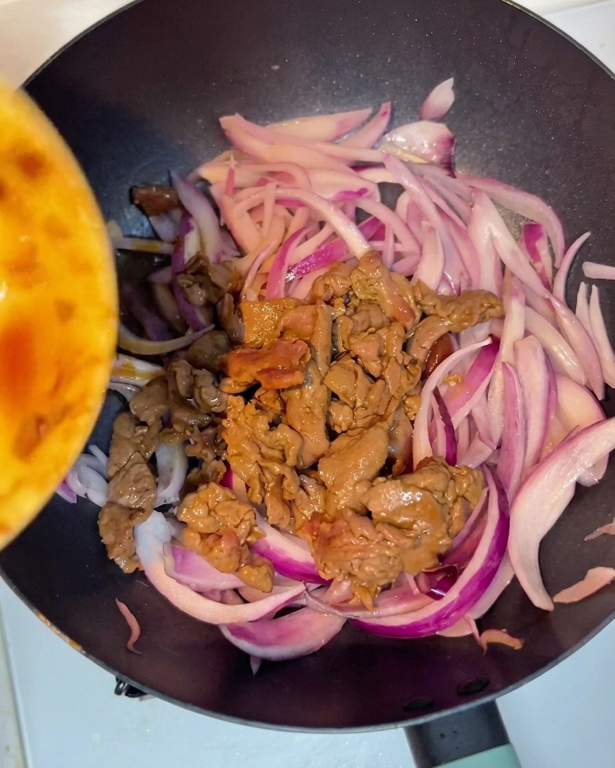 炒めた牛肉と赤玉ねぎがフライパンで混ざり合っている様子。