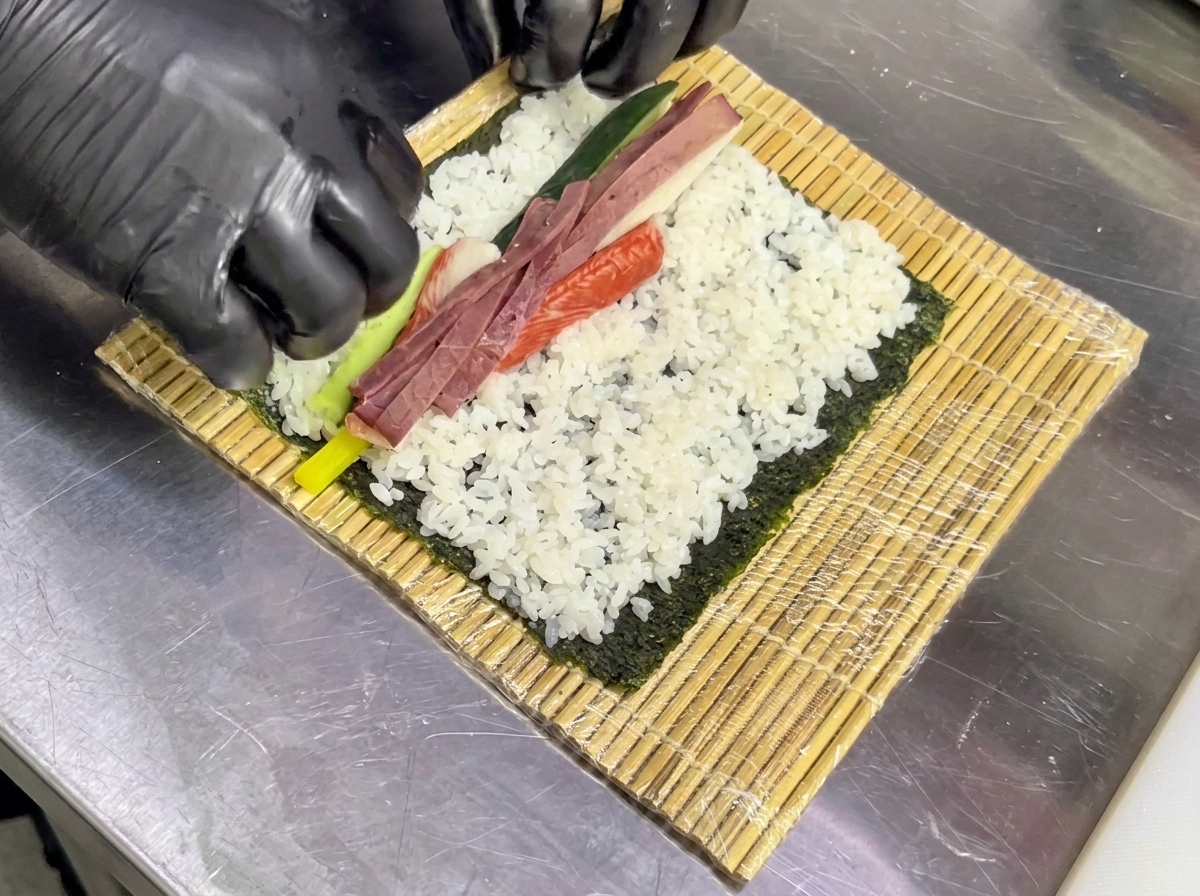 味付けしたご飯を広げた海苔の上に、丁寧に具材を並べている様子。