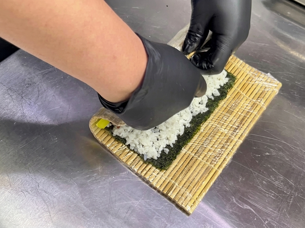 両手で巻きすを持ち、具材を包み込み始める様子。