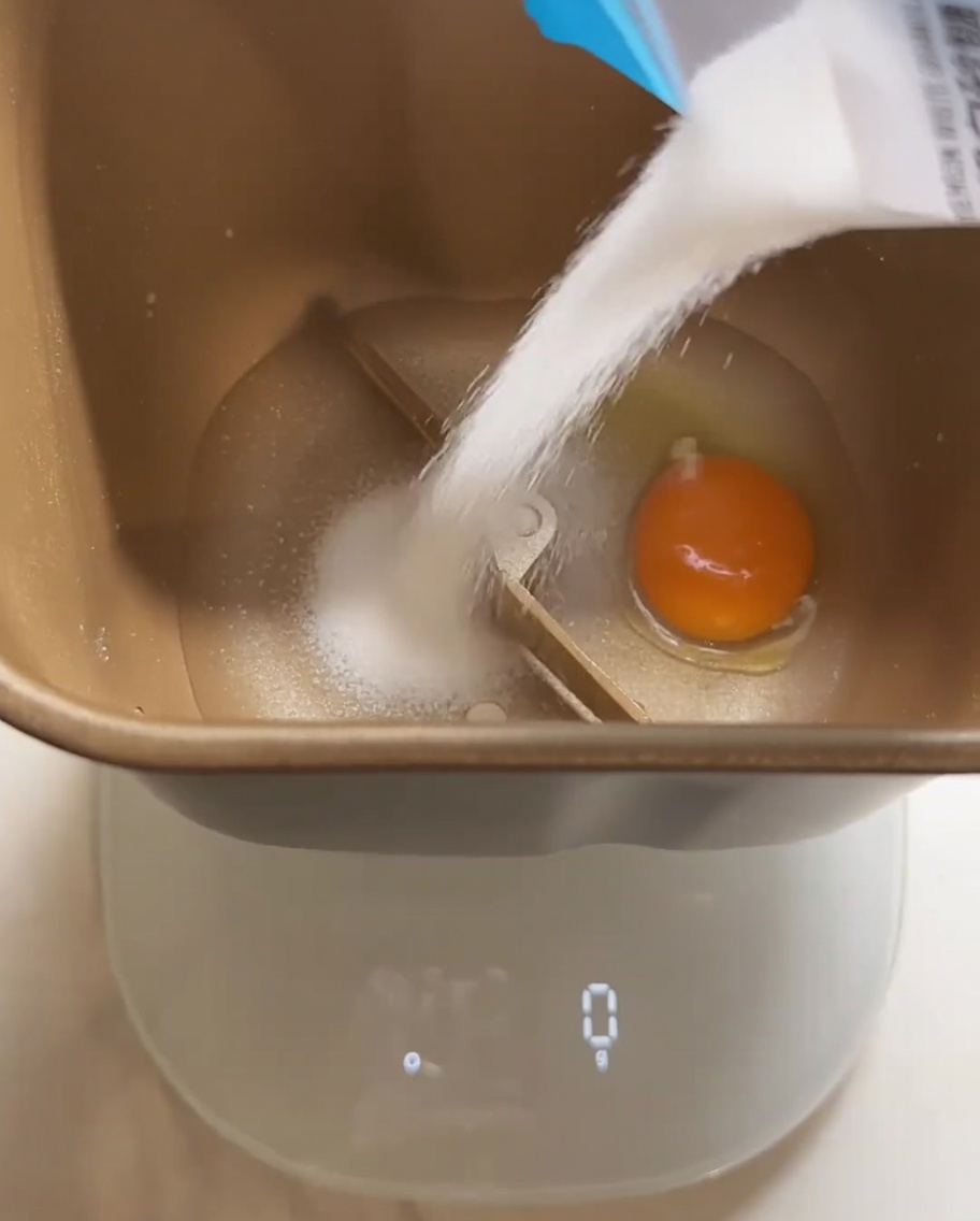 ホームベーカリーの容器に、卵や砂糖などのパン生地の材料を入れている様子。