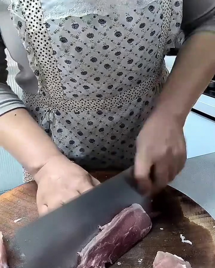 まな板の上で生の豚赤身肉を包丁で厚さ1cmに切り分けている様子。