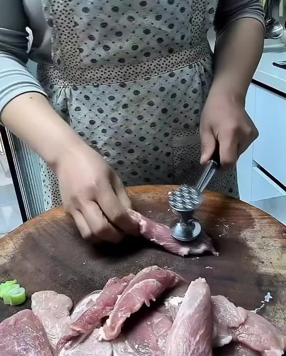 木製の台の上で、肉叩きを使って豚肉の切り身を薄く叩いている様子。