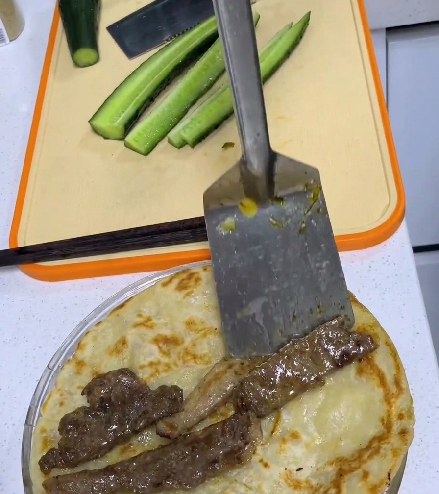 焼きたての葱油餅の上に、平らに広げた豚肉を置いている様子。