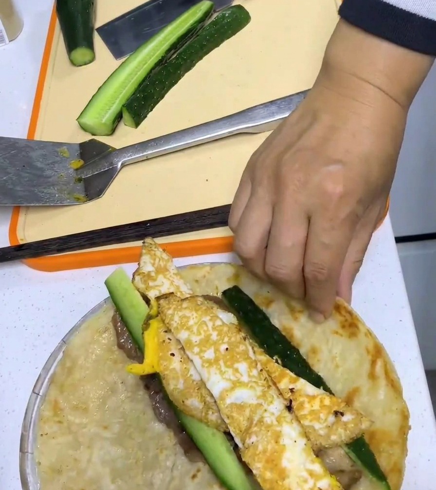 具材をのせた葱油餅をしっかりと巻いている手元の様子。