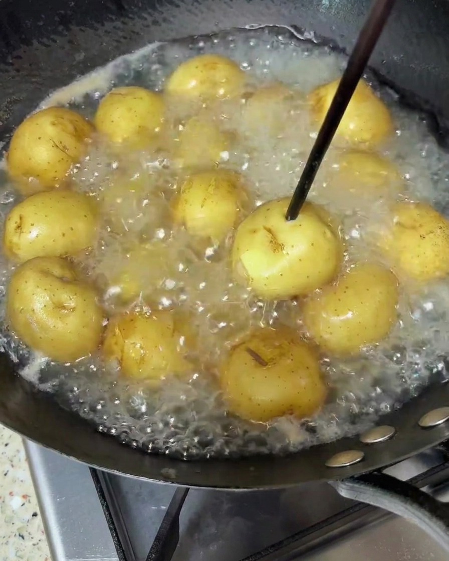 熱湯で茹でられているベビーポテトに、火の通りを確認するための菜箸が刺されている様子。