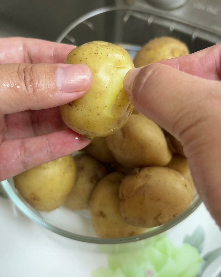 茹でたベビーポテトの薄い皮を手でむいているクローズアップ。