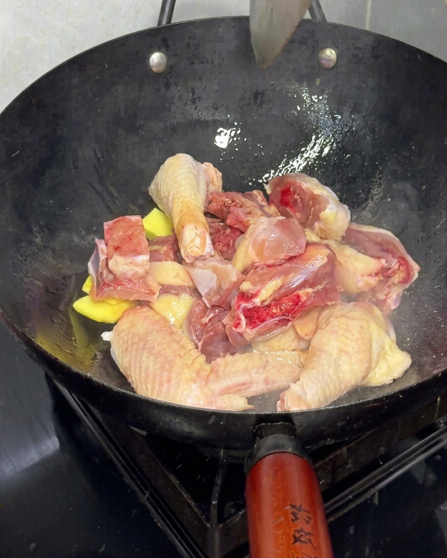 大きな中華鍋でショウガと一緒に鶏肉を炒めている様子。