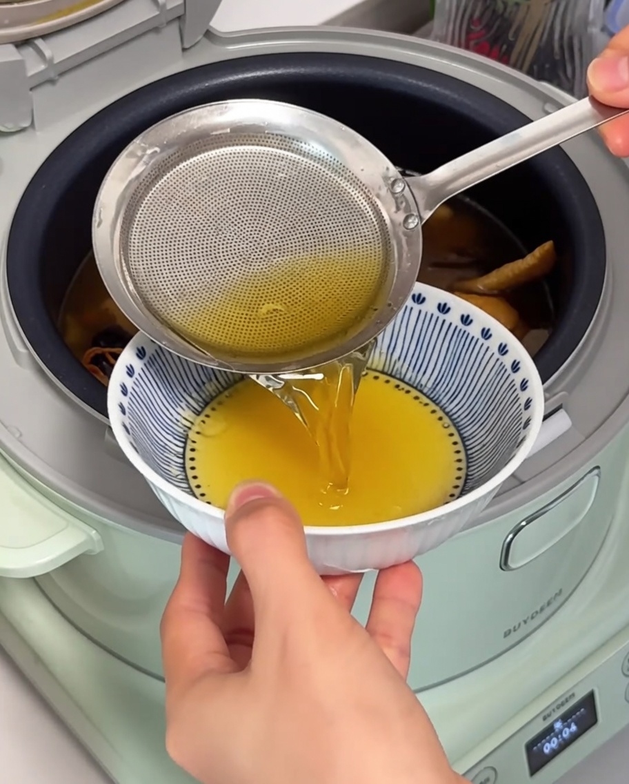 細かな網目のストレーナーでスープ表面の澄んだ鶏油をすくい取っている様子。