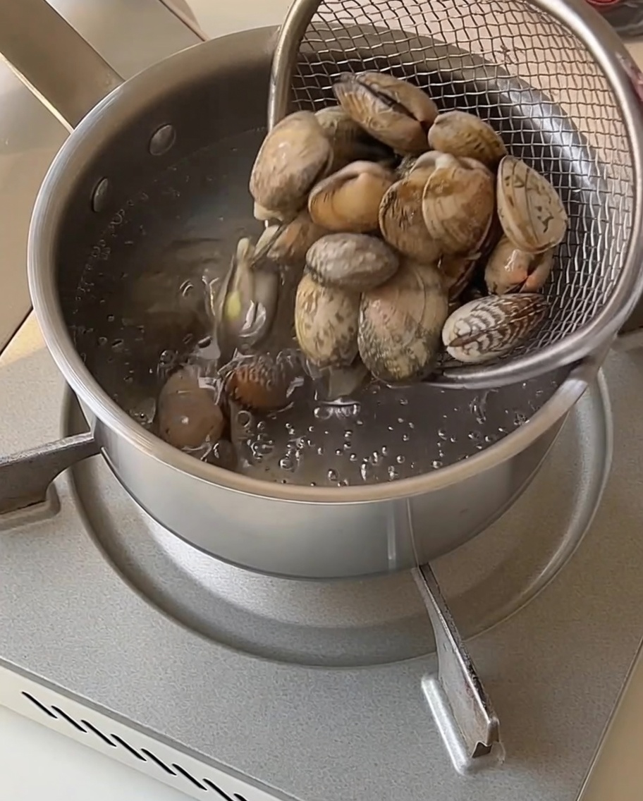 沸騰した鍋から網じゃくしでアサリを取り出している様子