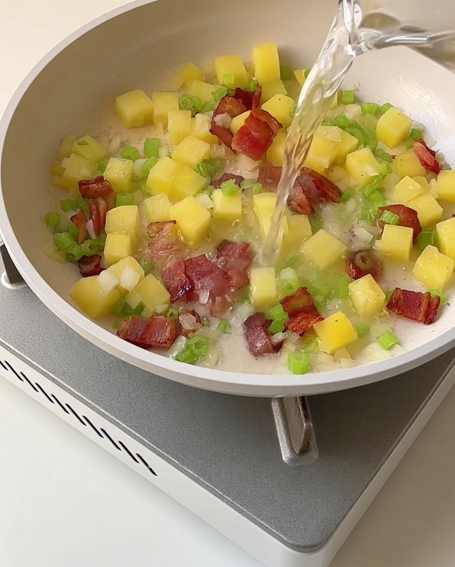 炒めた野菜とベーコンの入った鍋に透き通ったアサリの茹で汁を注ぐ様子