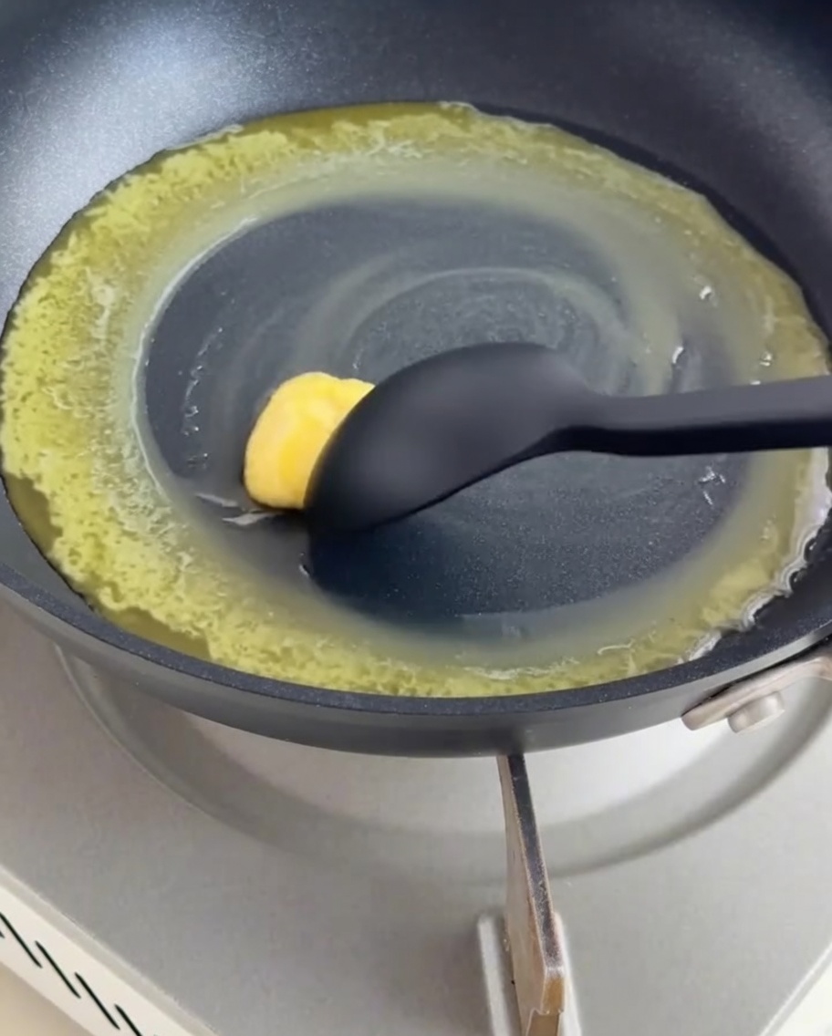 黒いテフロン加工のフライパンで、溶かしバターと小麦粉を黒いシリコンスパチュラで混ぜ合わせてルーを作っている様子。