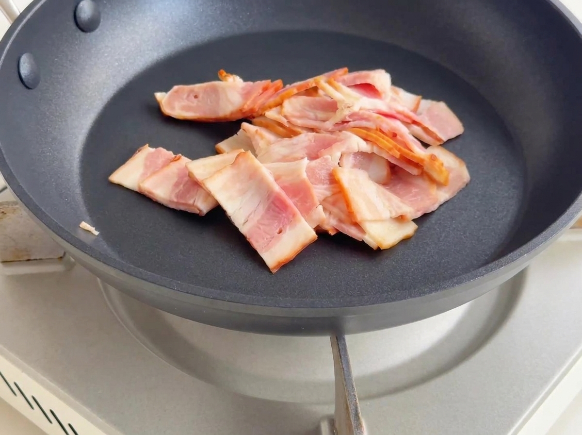 小さく切ったベーコンをフライパンで炒め、こんがりと焼き色がついて脂が出ている様子。