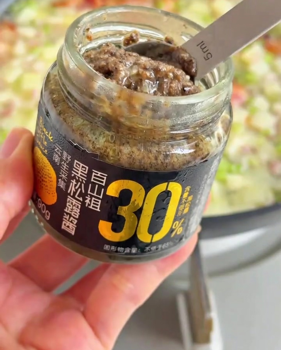 グツグツ煮立つ野菜とスープのフライパンに、スプーン1杯の黒いトリュフペーストを加えている様子。