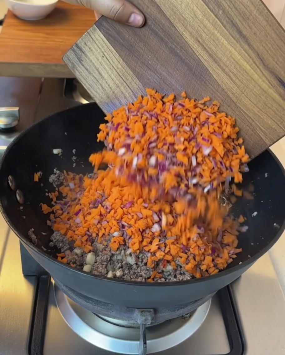 炒めた牛肉の入ったフライパンに、みじん切りにした野菜と角切りトマトを加えている様子。