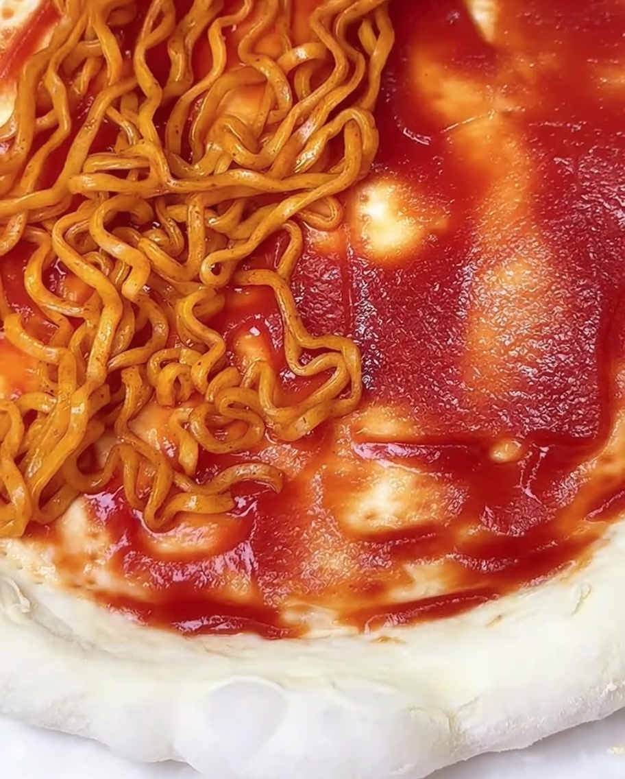 トマトソースを塗ったピザ生地に、スパイシーなラーメンと海苔をトッピングしているアップ画像。
