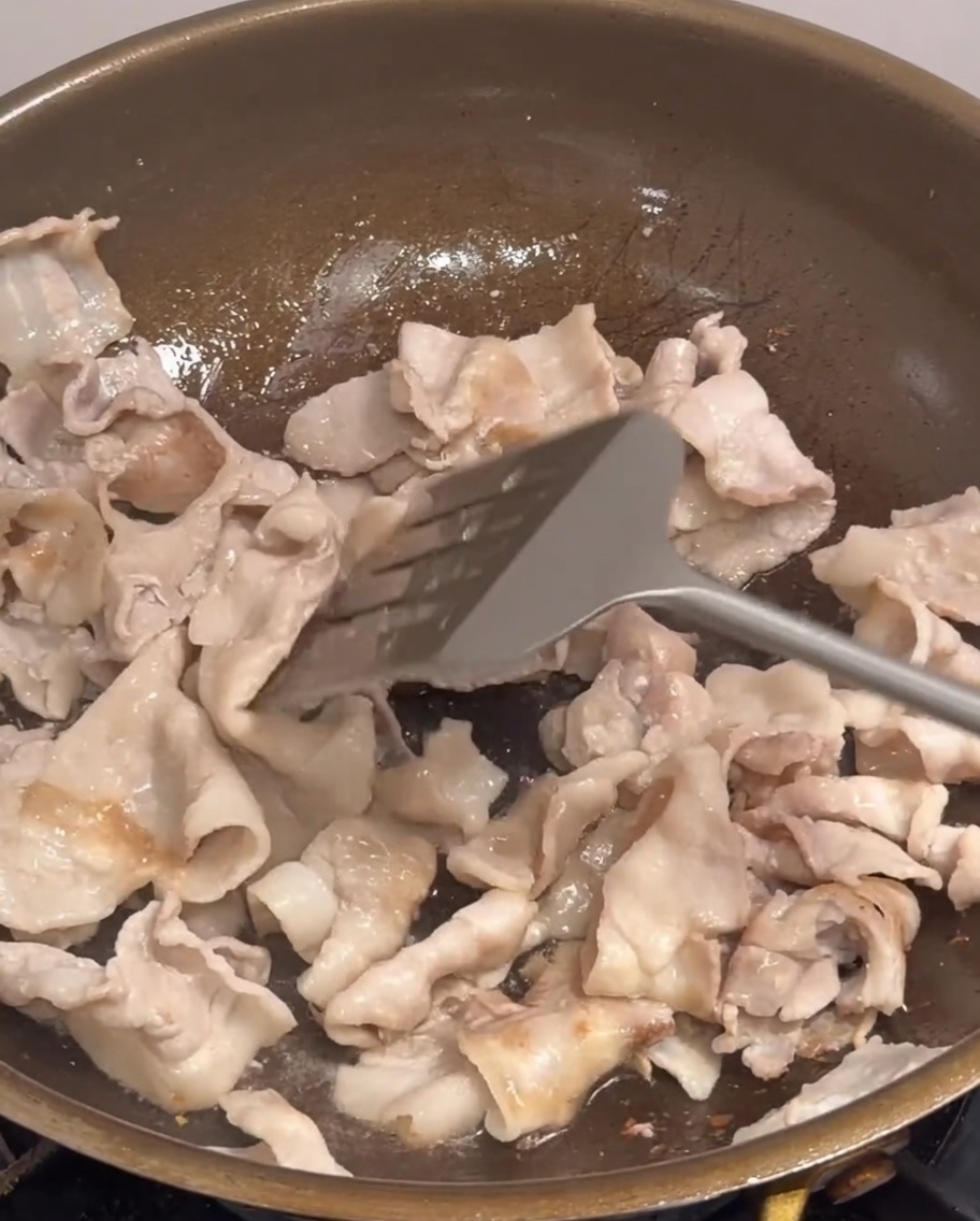 豚肉と一緒に玉ねぎ、長ねぎ、唐辛子を炒めている様子。