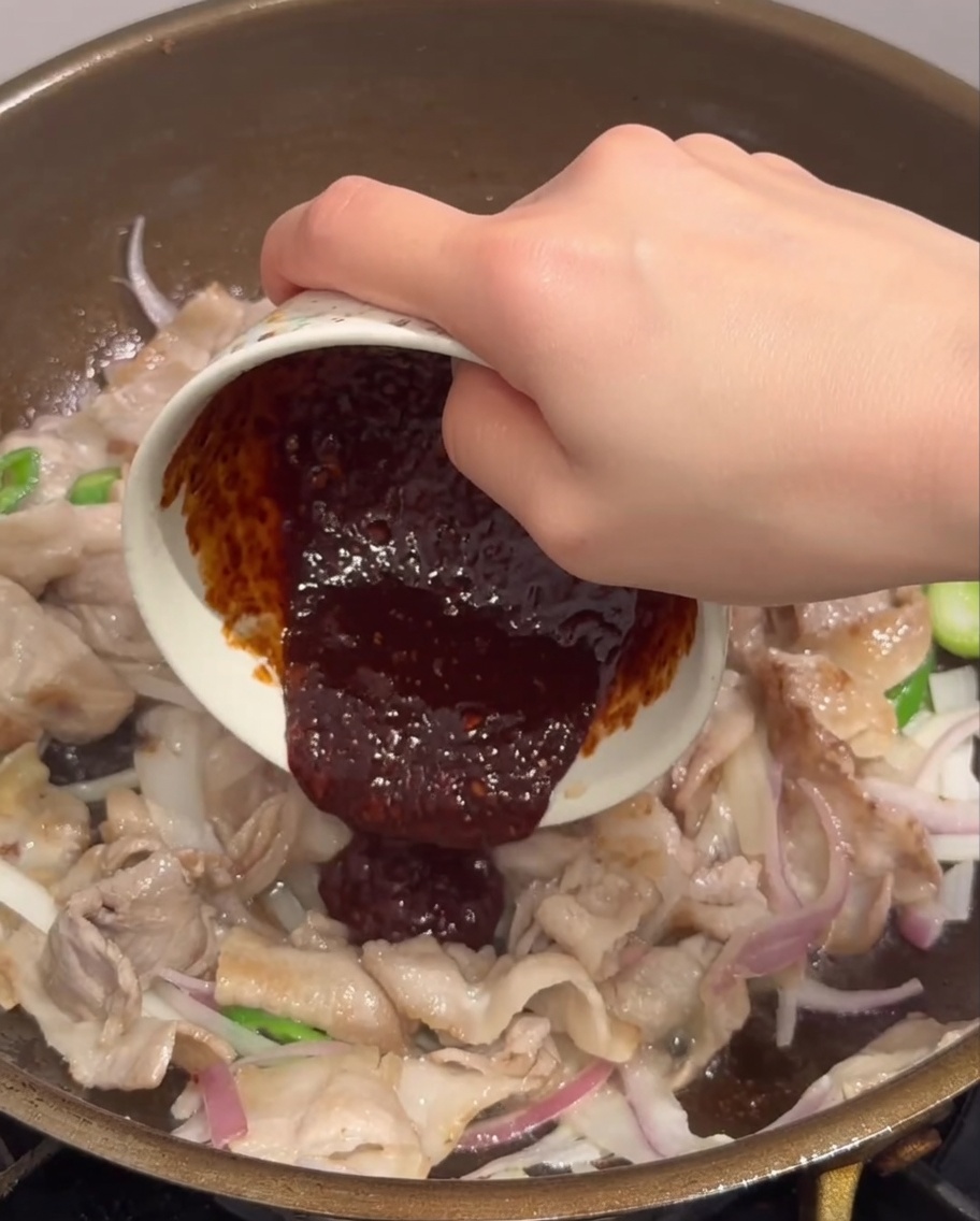 具材が入ったフライパンに、混ぜておいた合わせ調味料を注いでいる様子。