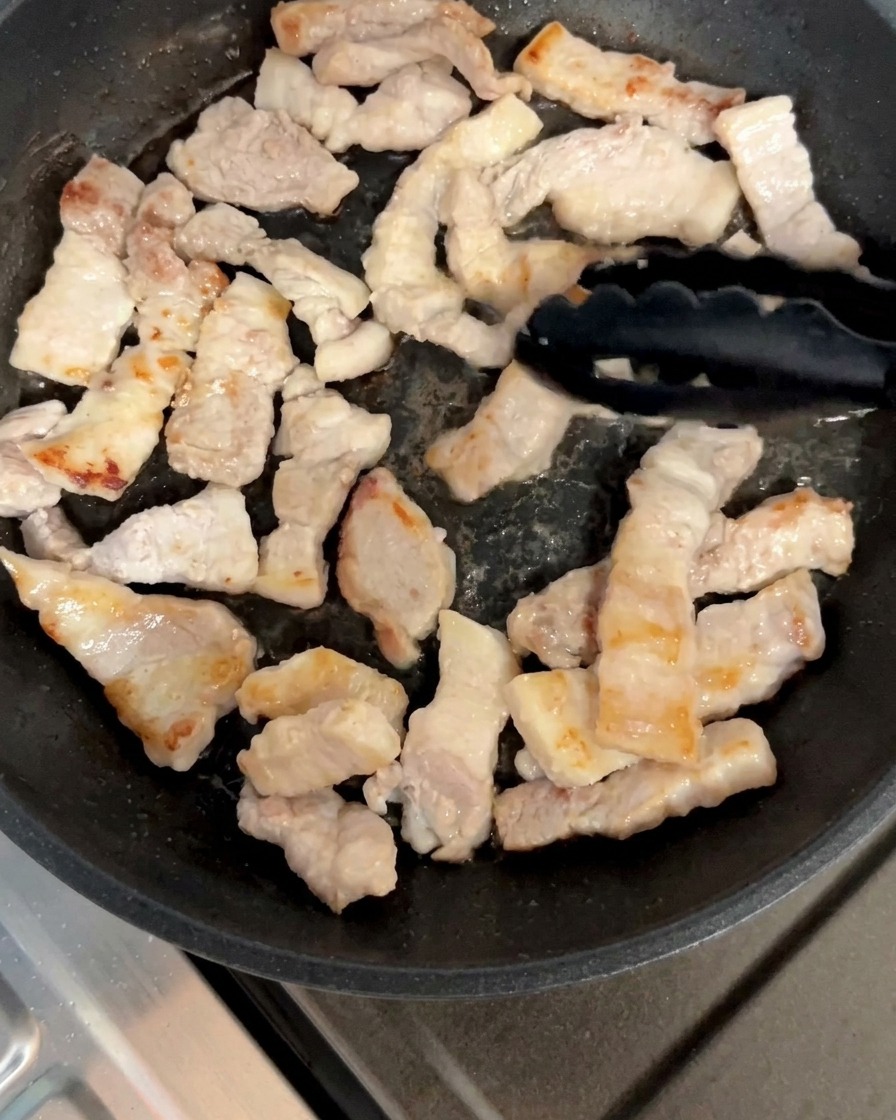 フライパンで豚バラ肉を両面がこんがりするまで焼いている様子。