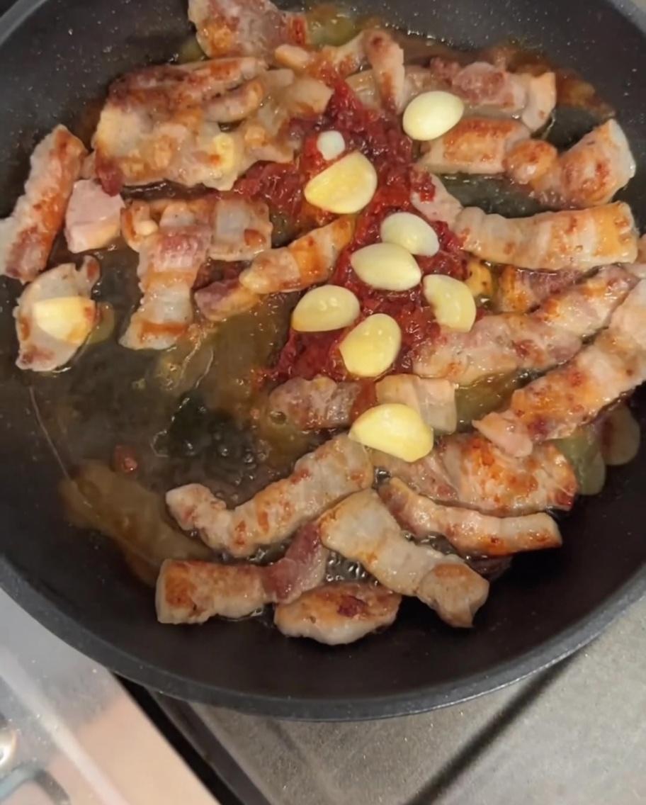 フライパンで豚肉とソース、ニンニクを炒め合わせている様子。