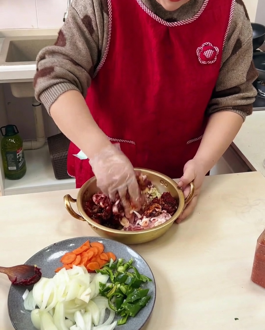 手袋をした手で、ボウルの中の豚肉とタレをしっかり混ぜ合わせている様子。