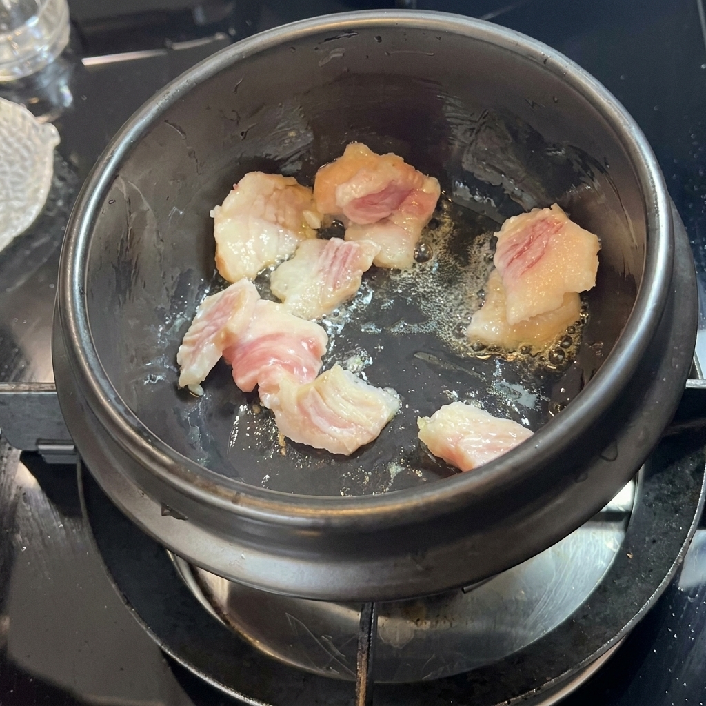 黒い石鍋で豚バラ肉を焼き、脂を引き出している様子。