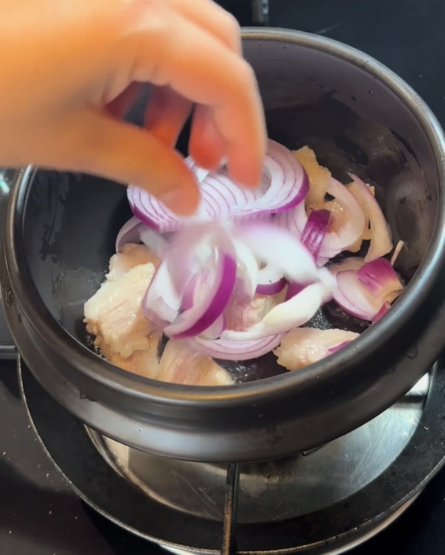 炒めた豚肉の入った鍋に紫玉ねぎのスライスを加えている様子。