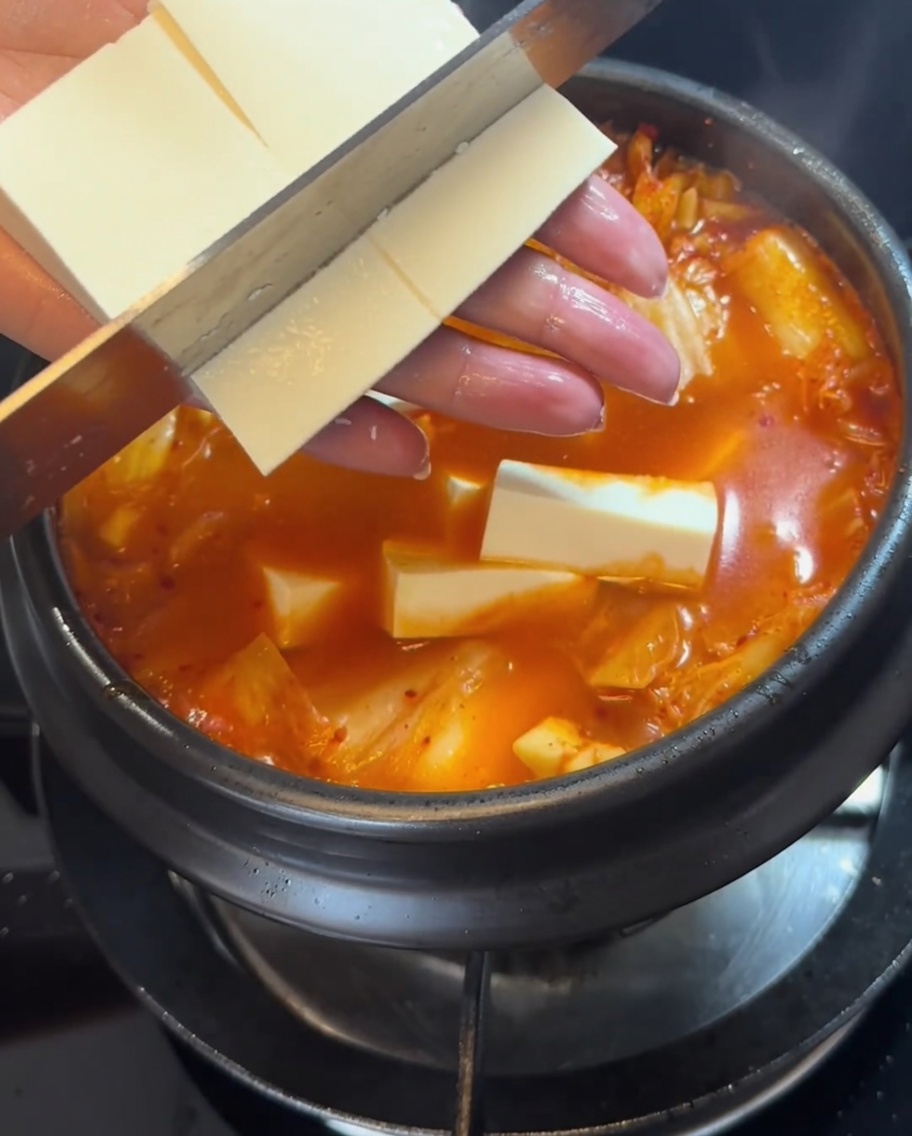 沸騰している赤いキムチチゲに、スライスした木綿豆腐をそっと入れている様子。