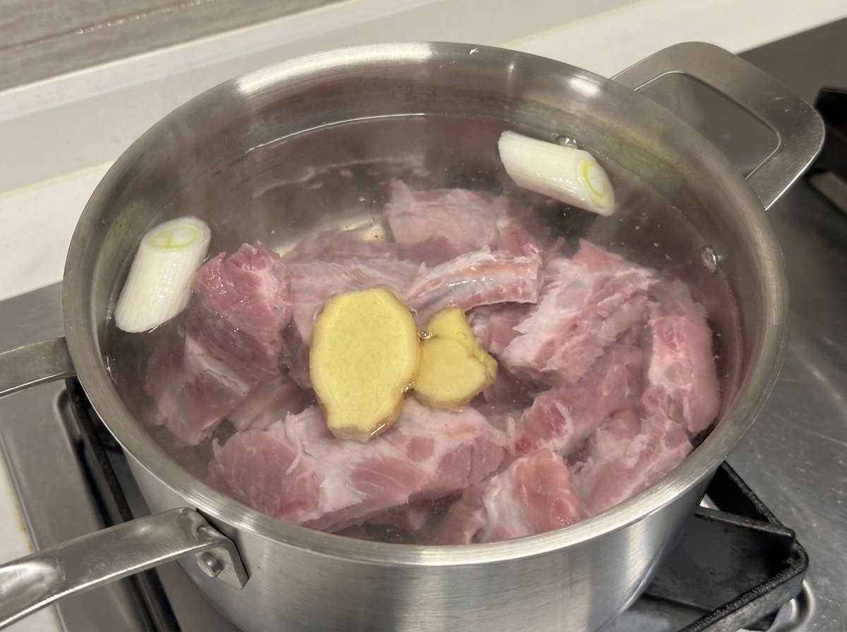 鍋に入った豚スペアリブ、長ねぎ、生姜、料理酒