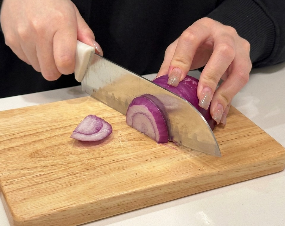 木製のまな板で赤玉ねぎを切る様子