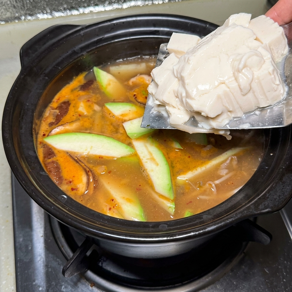 グツグツと煮える鍋に絹ごし豆腐を加える様子。