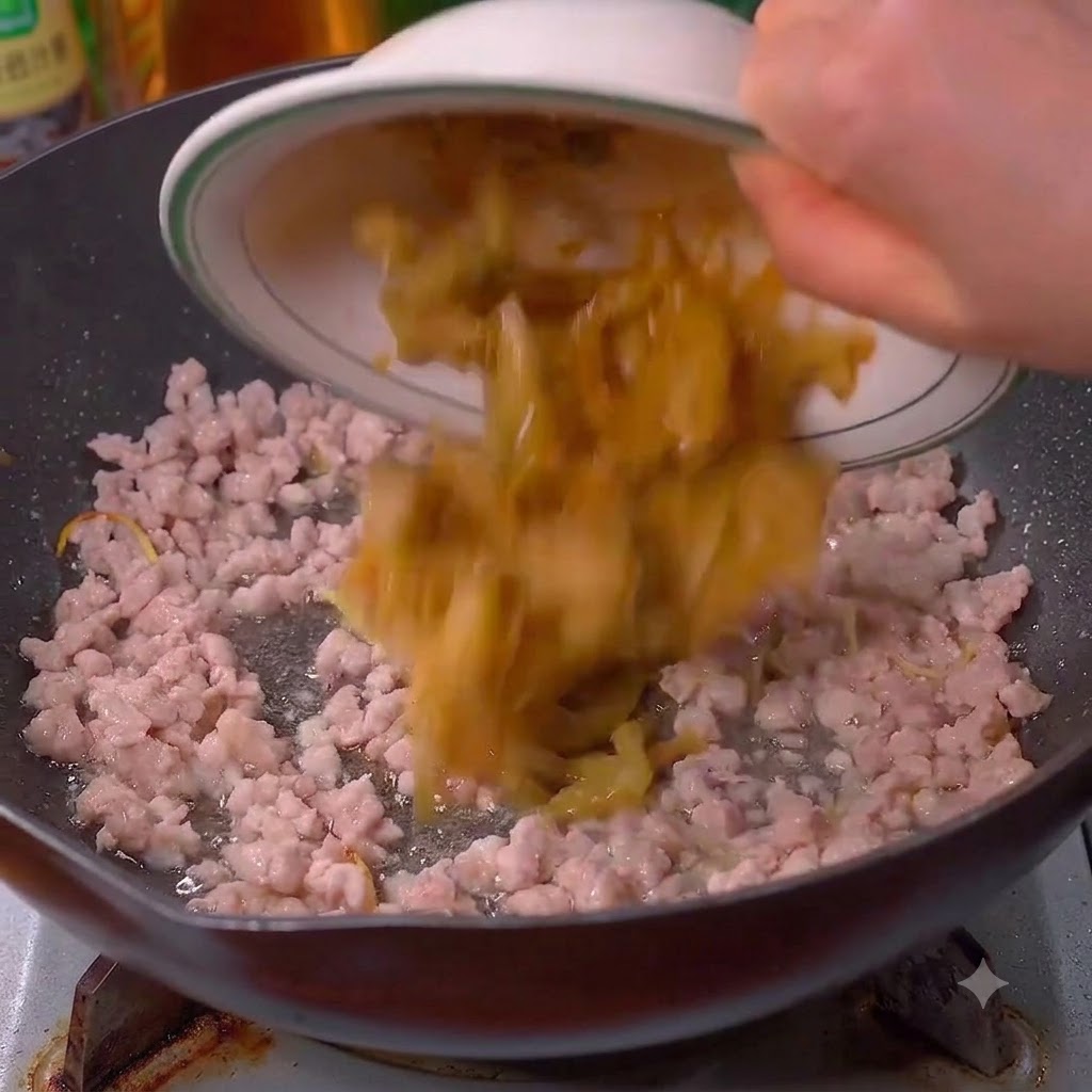 炒めた豚肉の入った中華鍋に高菜漬けを加えている様子。
