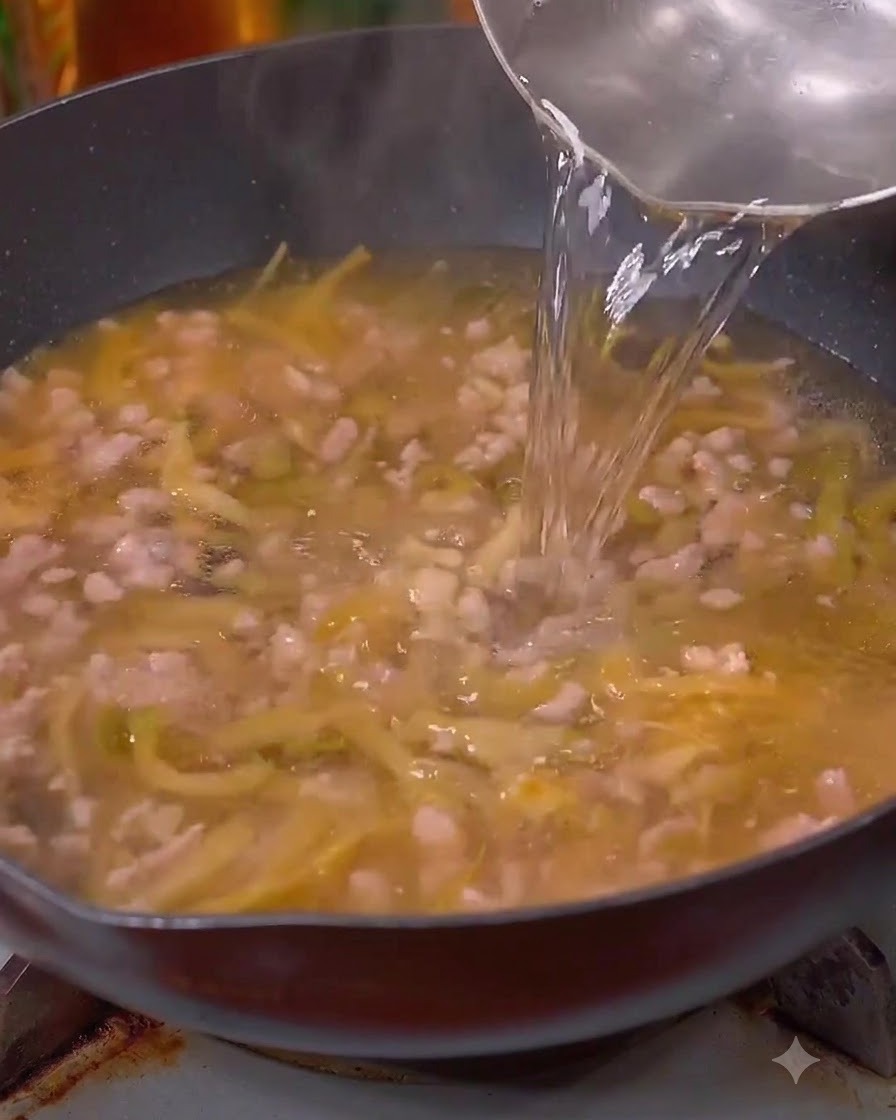肉と高菜の入った中華鍋に水を注いでいる様子。